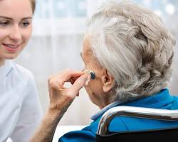 مشاوره سمعک: متخصص شنوایی‌شناسی با لبخند، در حال صحبت و راهنمایی یک بیمار میانسال پشت میز در کلینیک شنوایی سنجی.